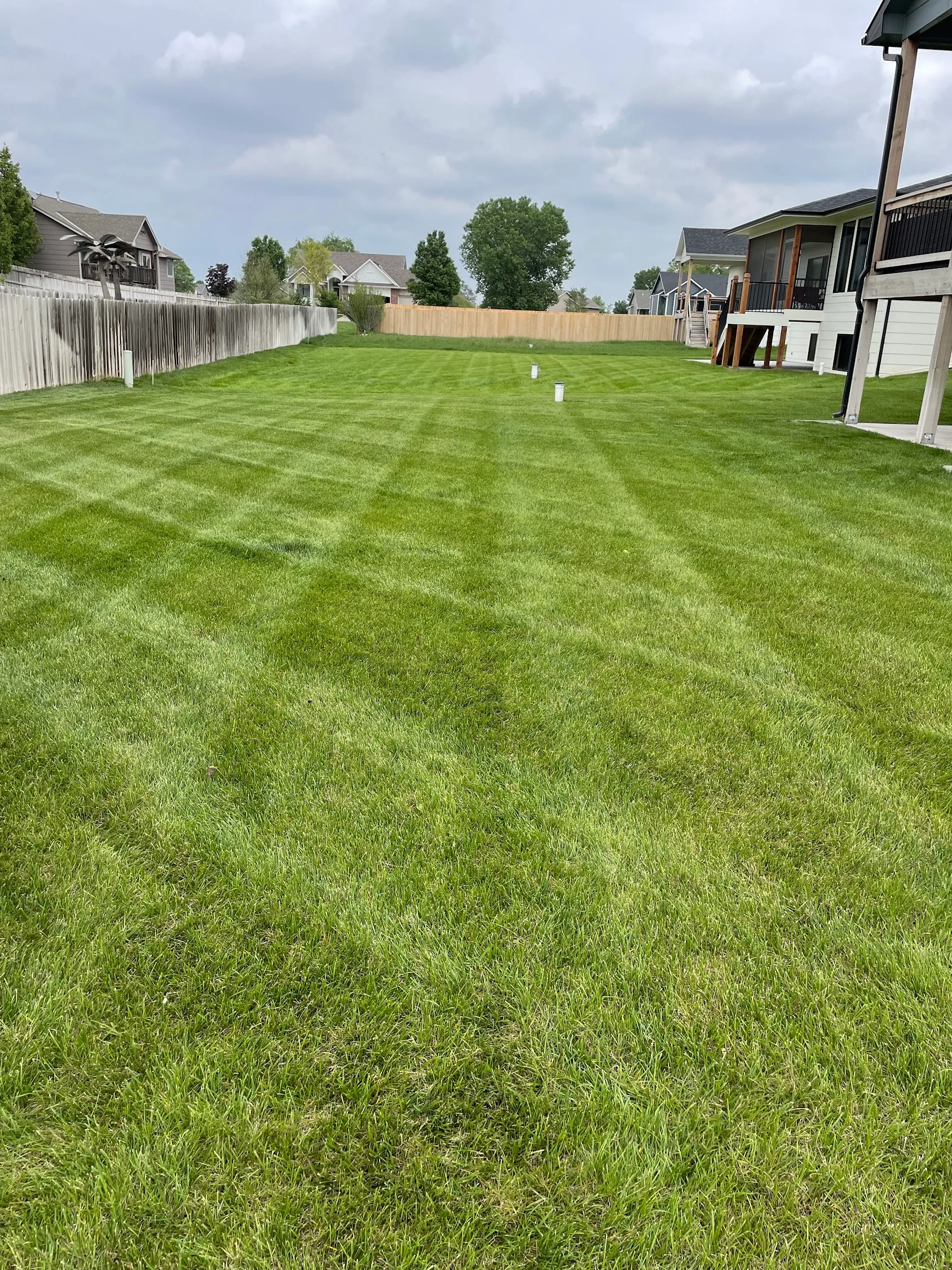 Dense green residential lawn with white and wood fencing, irrigation markers, and mature trees