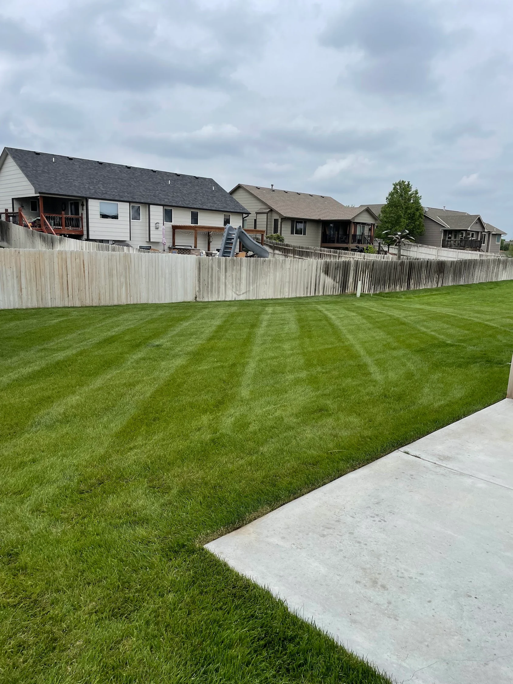 Striped lawn with professional mowing patterns, concrete walkway, and white vinyl fence