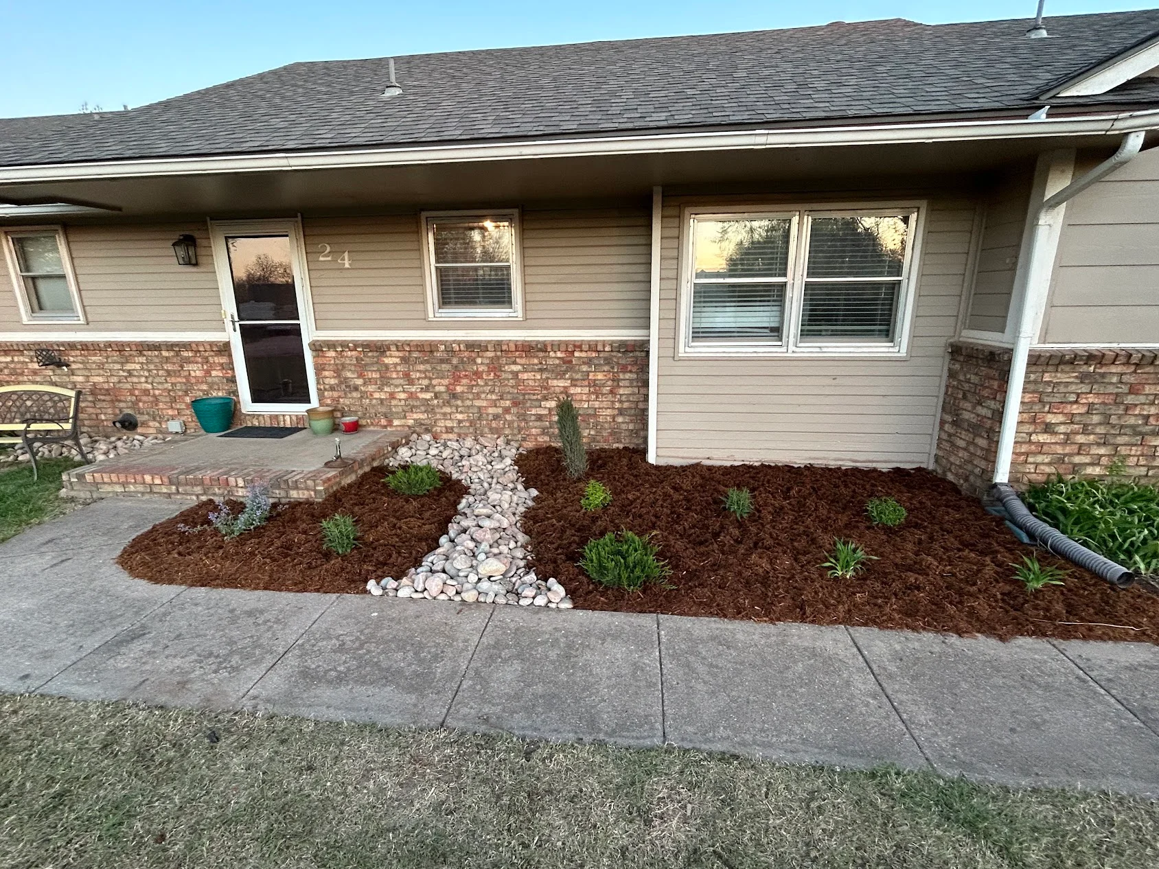 Front yard landscape beds with brown mulch, white river rock, and new plantings along brick foundation