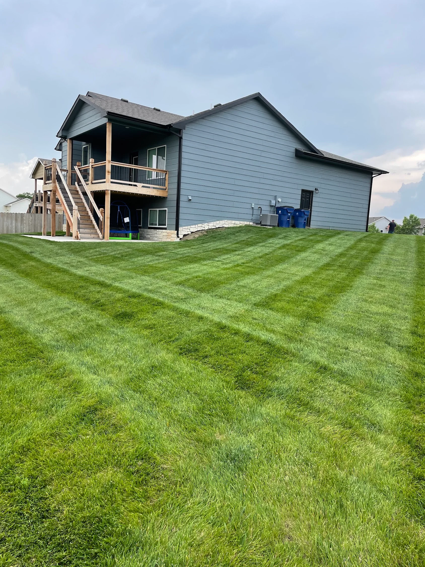 Striped lawn with healthy green grass in front of two-story residential home with deck