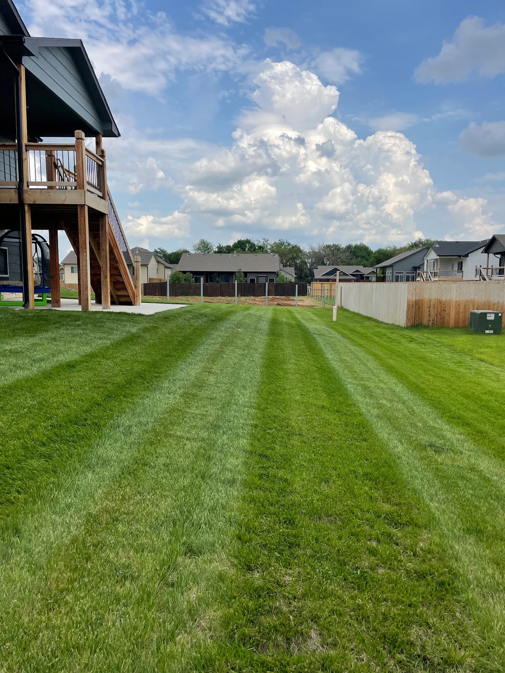 Striped lawn mowing pattern on residential yard with green grass and white fence