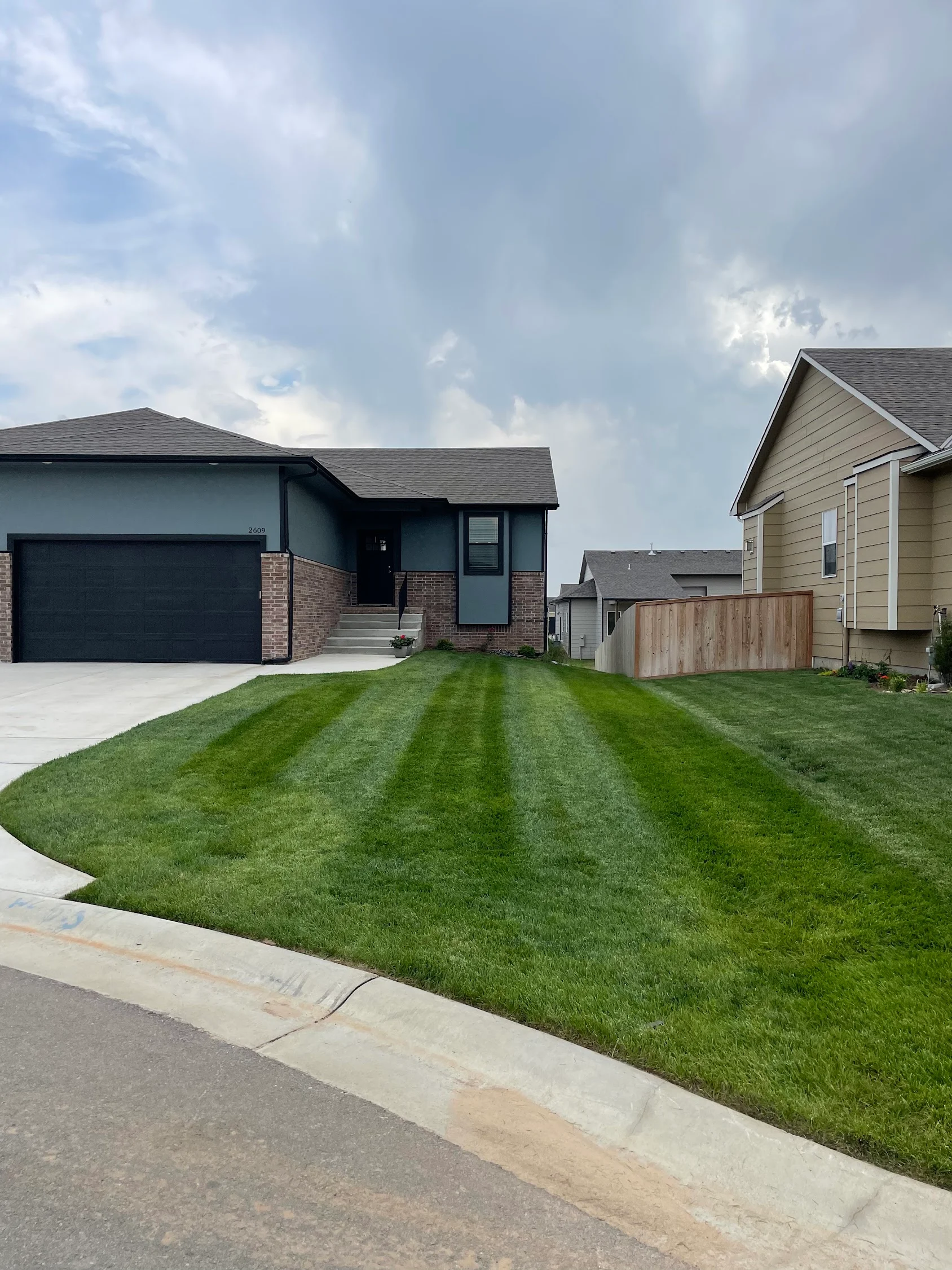 Newly installed sod lawn with professional striping on residential property with brick home and concrete driveway