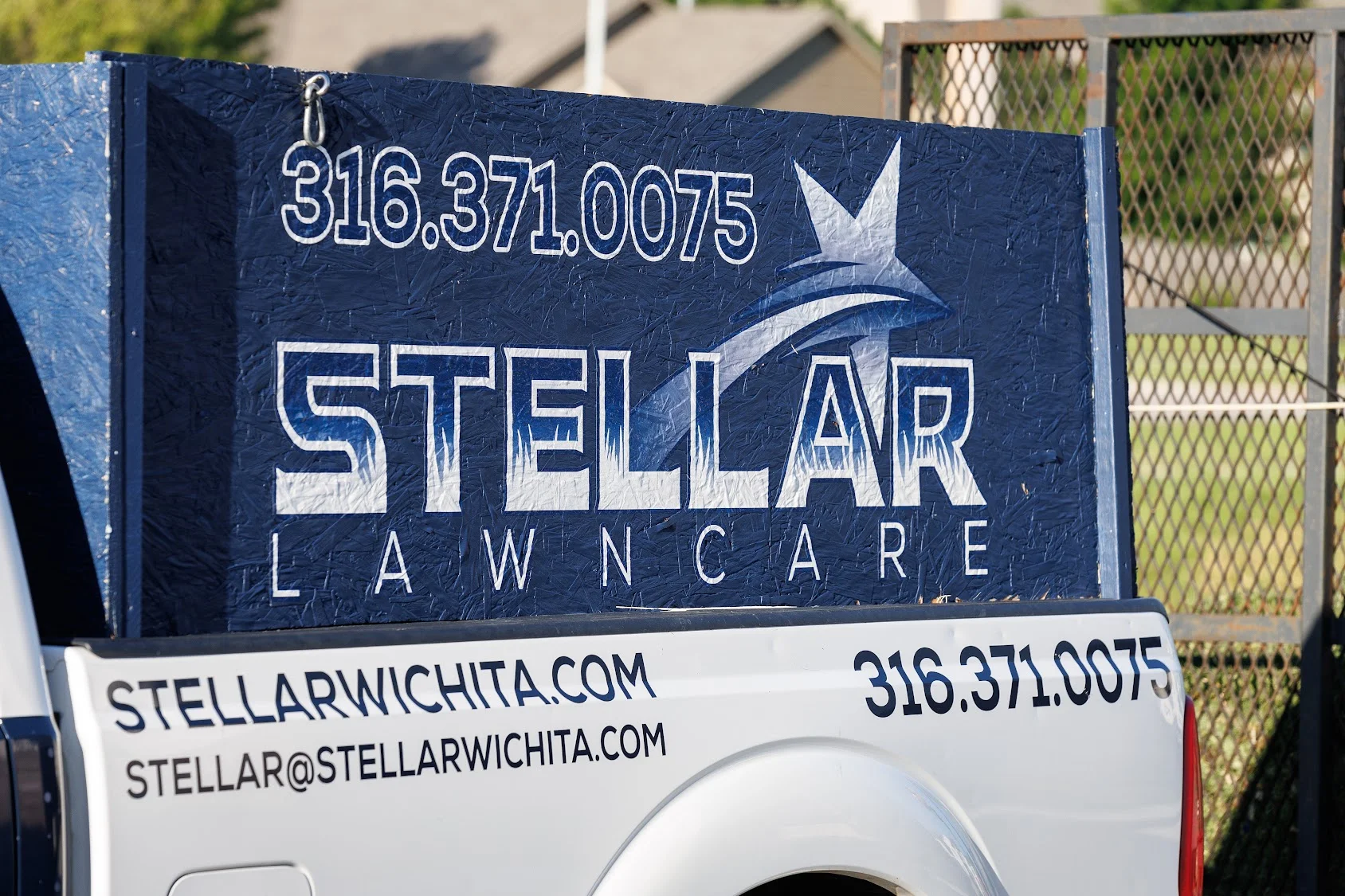 Navy blue vehicle sign with white lettering, fish logo, and business contact information for lawn care service