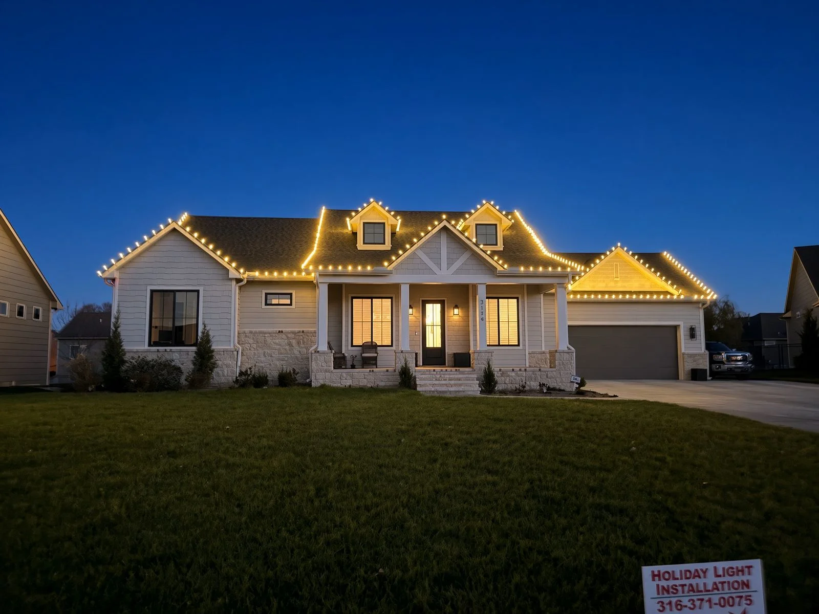 A Wichita residential home with evenly spaced holiday lights mounted along the full roofline and gutters, with wrapped shrubs visible in the front yard. The display is photographed at dusk against a Kansas winter sky.