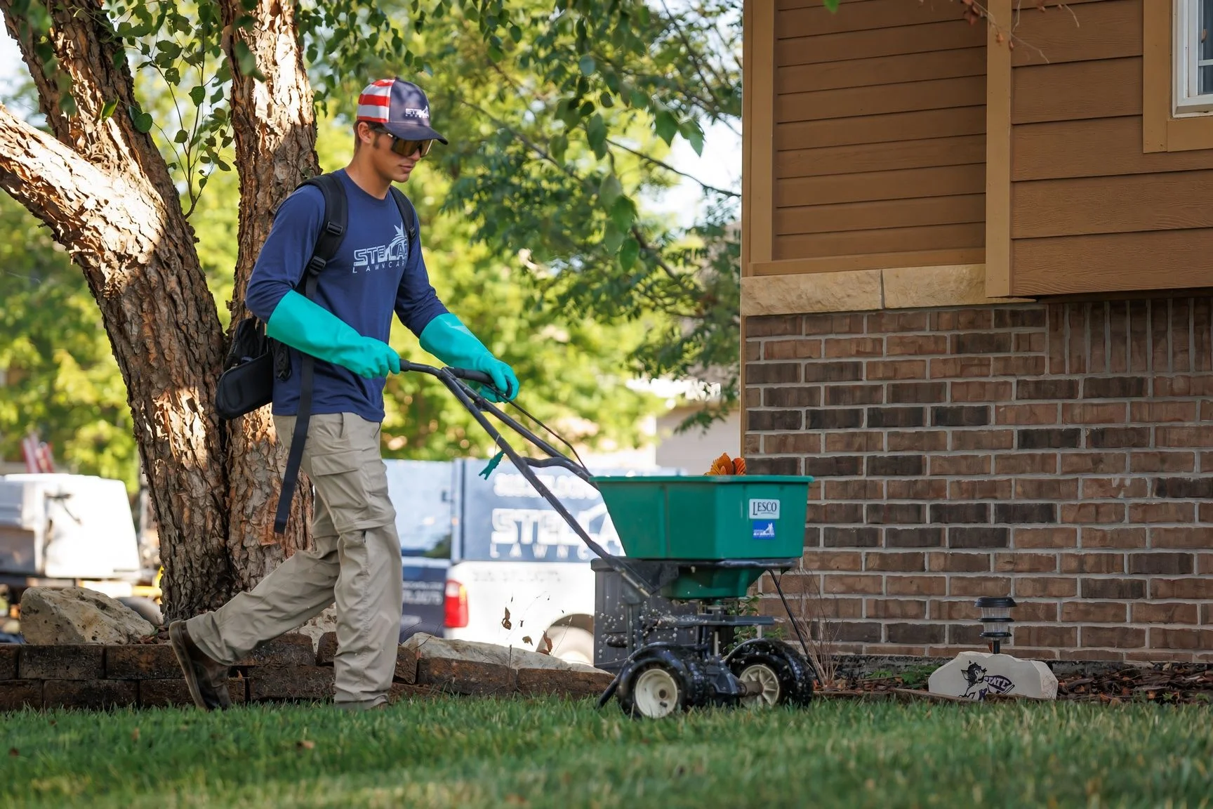 A Stellar Lawn Care LLC technician applying lawn fertilization treatment to a thick, green residential yard in Wichita, Kansas. The lawn shows even color and dense turf growth typical of a well-maintained cool-season grass property in the Wichita area.