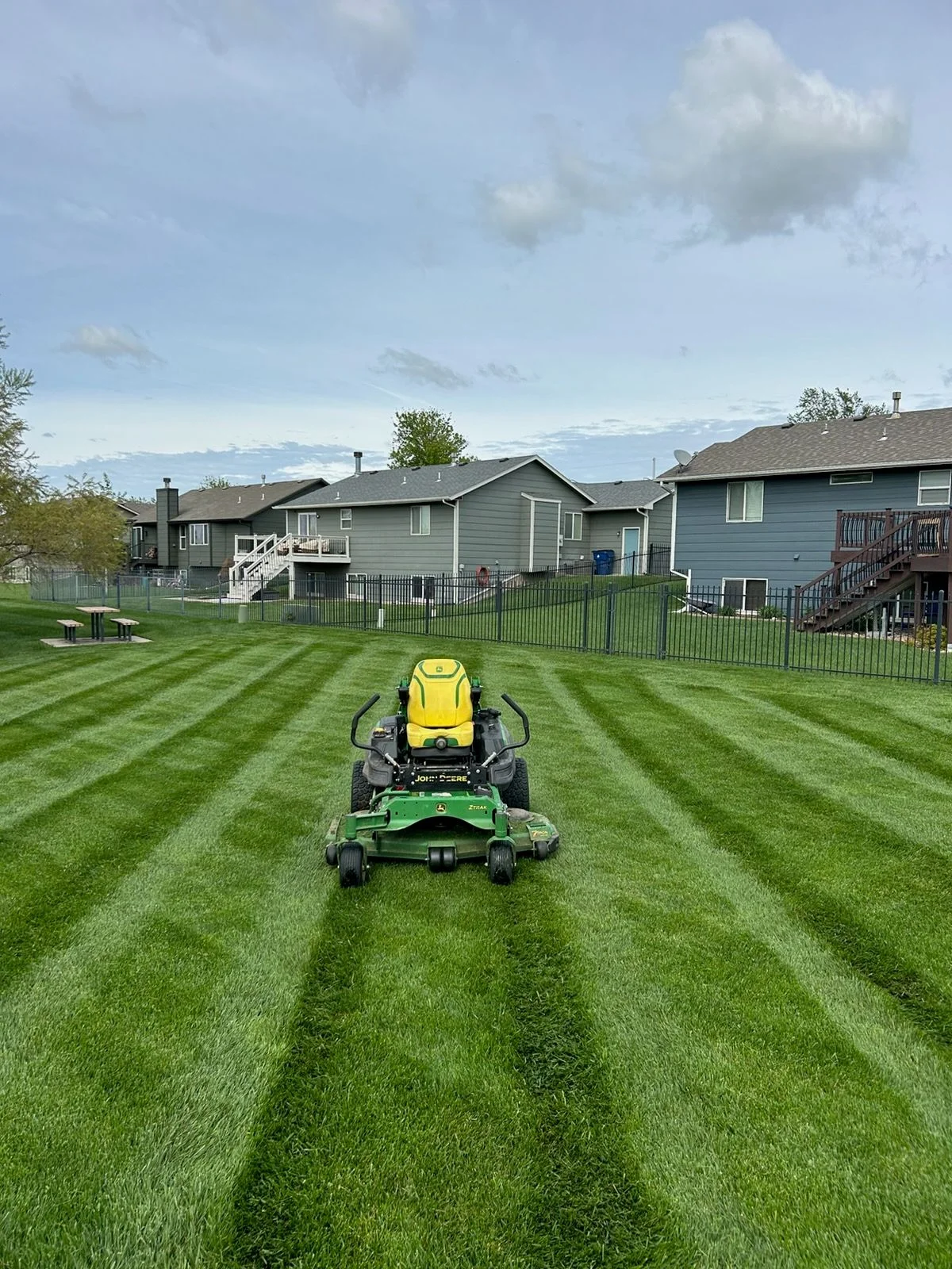 A freshly mowed residential lawn in Wichita, Kansas, with clean mow lines, trimmed edges along a concrete driveway, and no clippings on the walkway. The grass is an even height with no brown patches visible.